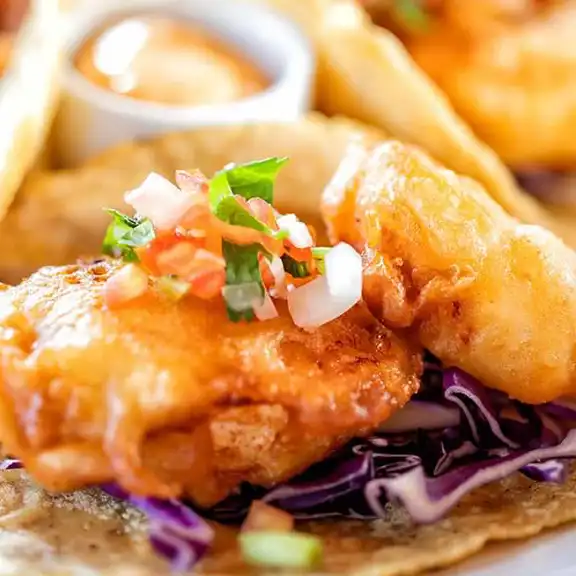 Crispy fried fish taco topped with purple cabbage slaw and pico de gallo